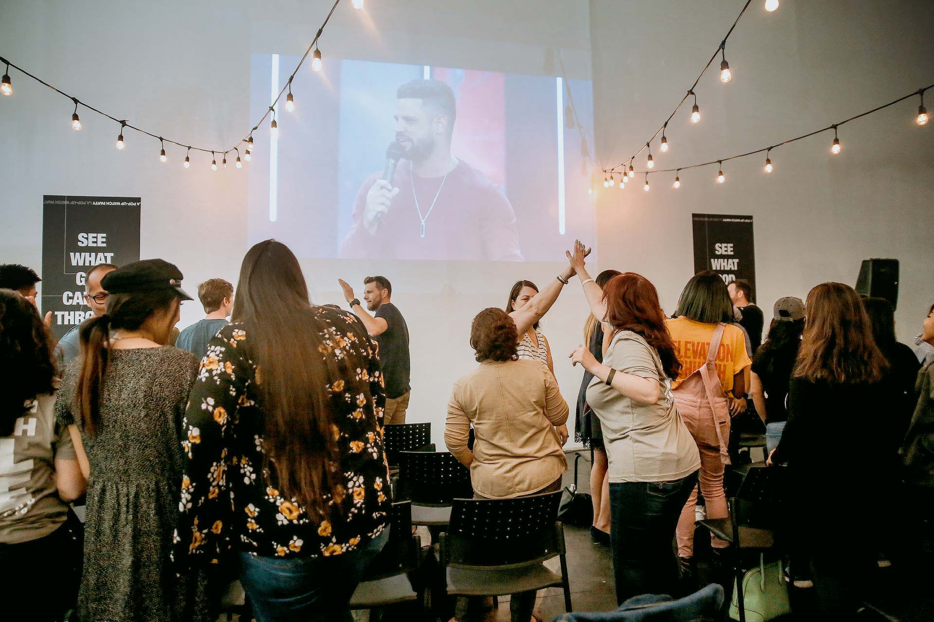 A group of people greeting each other while watching Pastor Steven Furtick at a watch party